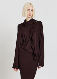 Dark brown long-sleeve top with asymmetrical ruffle detail, soft texture, and elongated sleeves, paired with a fitted skirt.