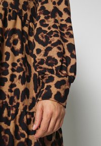 Main de femme reposant à côté d'une robe à manches longues imprimée léopard avec poignet froncé et couture à étages.