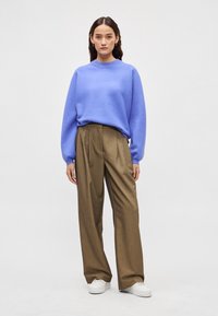 Ανοιχτό μπλε πουλόβερ πλεκτό με λαιμόκοψη, συνδυασμένο με ψηλόμεσα, καφέ παντελόνια φαρδιάς γραμμής και λευκά αθλητικά. Απλός σχεδιασμός και υφή.