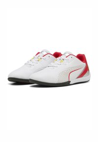 Zapatos deportivos blancos con acentos rojos, paneles texturizados y suelas negras. Presentan cordones amarillos y un diseño perforado para permitir la transpirabilidad.
