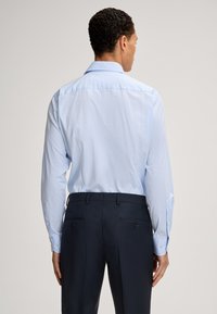 Camicia azzurro chiaro a maniche lunghe con colletto classico e polsini abbottonati, abbinata a pantaloni scuri in navy su misura con tasche posteriori.
