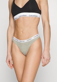 G-string Calvin Klein in cotone grigio chiaro con una vita elastica bianca a contrasto che presenta un logo nero, design a vita bassa e texture liscia.