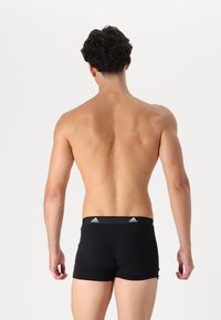 Juodos Adidas boxer šortai, kurie puikiai priglunde, turi glotnią tekstūrą ir elastingą juosmenį su logotipo akcentu. Rodoma nugarinė pusė.