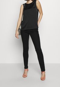 Svart satinlinne utan ärmar kombinerat med svarta skinny jeans, kompletterat med korallfärgade remsandaler och en silverkedjehandväska.