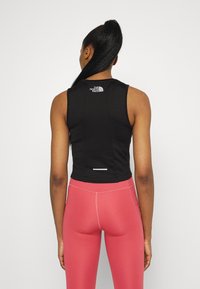 Black sleeveless crop top with logo on back, paired with pink high-waisted leggings. Smooth material, fitted design, and contrasting colors.