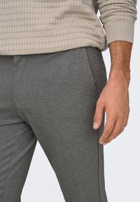 Pantalon texturé gris à coupe ajustée, doté de poches latérales et d'une finition lisse, porté avec un pull en tricot beige.
