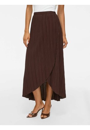 Brun plisseret omslagsnederdel båret med brune hælede sandaler og en hvid top, vist fra taljen til fødderne på en stående person.