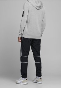 Suéter gris con capucha y tejido texturizado, combinado con pantalones joggers negros con detalles blancos. El calzado es una mezcla de blanco y gris.