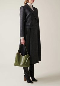 Grau karierter, doppelt geknöpfter Blazer mit passendem Rock, kombiniert mit einer grünen Ledertasche und schwarzen kniehohen Stöckelschuhen.