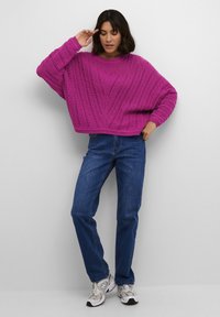 Maglione lavorato a maglia di un vivace rosa con una vestibilità comoda, caratterizzato da un motivo testurizzato e polsini a coste, abbinato a jeans di denim blu e sneakers grigie.
