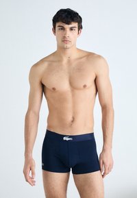 Navy blue boxer briefs with elastic waistband featuring a white logo. The fabric is smooth, fitted, and extends mid-thigh.