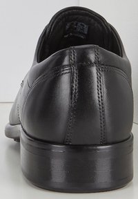 Scarpa in pelle nera vista dal retro, con una superficie liscia, cuciture sottili e un tacco basso e testurizzato. Prodotta in Portogallo.