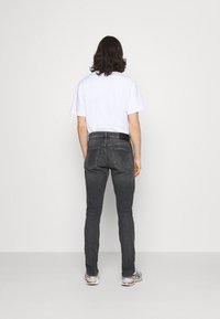 Svarta denimjeans har en taperad passform med bakfickor och är tillsammans med en enkel vit t-shirt. Outfiten kompletteras av sportiga sneakers.