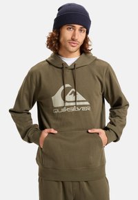 Olivengrøn hættetrøje lavet af blødt stof, med en forlomme og et stort hvidt Quiksilver-logo på brystet.