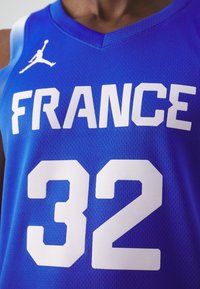 Maglia da basket blu con la scritta "FRANCIA" in grandi lettere bianche e il numero "32" in bianco, realizzata in un materiale in mesh traspirante.