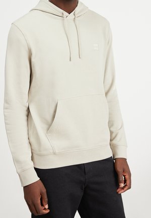 Sudadera de color beige claro, hecha de una tela suave, con un bolsillo tipo canguro, capucha con cordón y un pequeño parche con el logo en el pecho.