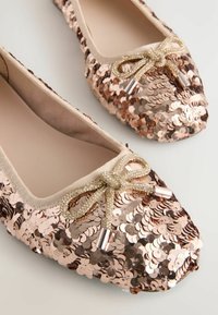 Balletflats mit Pailletten und abgerundeter Zehenpartie, bedeckt mit roségoldenen Pailletten und einem dekorativen, mit Perlen verzierten Schleifendetail an der Vorderseite. Glatte Innenauskleidung.