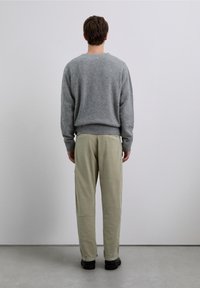 Suéter de lana gris con cuello redondo, combinado con pantalones entallados color caqui claro. Ambas prendas tienen un ajuste relajado y un diseño minimalista.