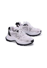 Scarpe sportive bianche con accenti neri, tomaia in rete e materiale sintetico, suola in gomma spessa e design con lacci, caratterizzate da un tassello sul tallone.