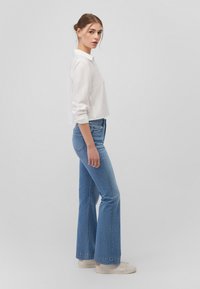 White, long-sleeve collared shirt paired with light blue flared jeans and white sneakers. The outfit features a casual fit and soft textures.