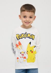 Maglietta bianca a maniche lunghe con grafiche colorate dei Pokémon: Pikachu e Scorbunny, con il testo "Pokémon" in lettere blu grasse sul petto.
