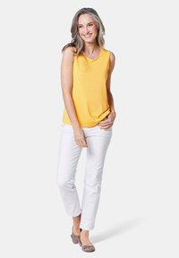 Top giallo senza maniche con scollatura rotonda, abbinato a pantaloni bianchi. L'outfit presenta una vestibilità comoda e una texture del tessuto liscia.