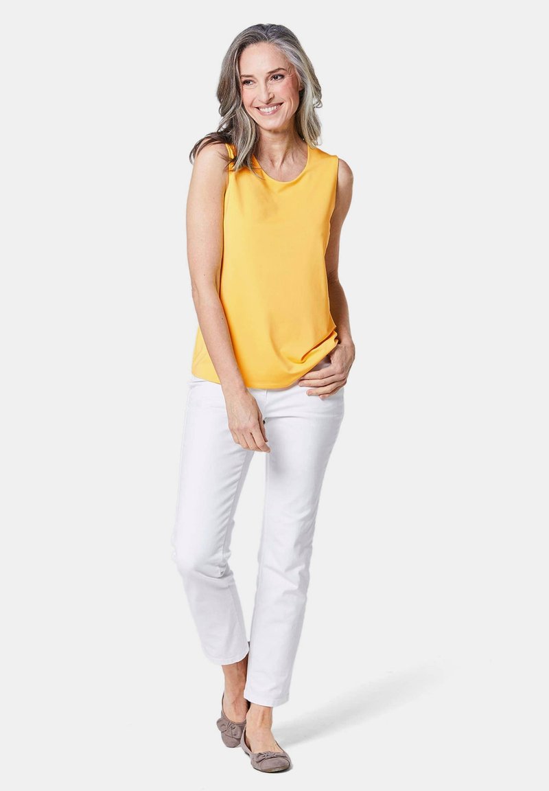 Top giallo senza maniche con scollatura rotonda, abbinato a pantaloni bianchi. L'outfit presenta una vestibilità comoda e una texture del tessuto liscia.