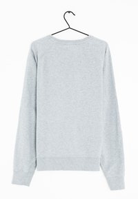 Sweatshirt en coton gris à manches longues, avec un col rond côtelé et des poignets. Texture lisse, design basique, suspendu à un crochet noir.