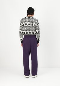 Black and white patterned sweater with leaf motifs paired with loose-fitting purple pants. Model wears a black beanie.