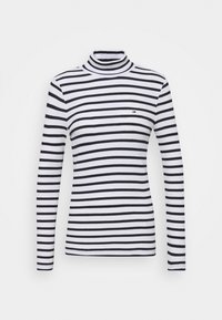 Maglione a collo alto a righe bianche e nere con maniche lunghe, realizzato in tessuto morbido. Presenta un piccolo logo sul petto. Design classico aderente.