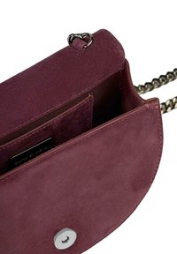 Burgundowa zamszowa torebka na ramię z srebrnymi akcentami, z łańcuszkowym paskiem, zapięciem na klapkę oraz wewnętrznymi kieszonkami na karty. Miękka tekstura i okrągły kształt.