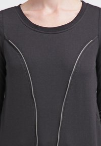 Svart sweatshirt med rundad halsringning och kontrasterande silverfärgad dragkedjedetalj längs de främre sidorna. Mjuk, texturerad tyg.