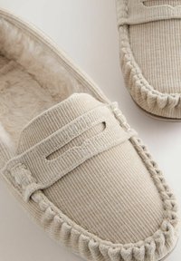 Beige corduroy moccasin-slippers met een pluche voering en decoratieve stiksels op de randen. Voorzien van een gestikt uitsnede nabij de teen.