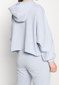 Felpa corta azzurro chiaro con cappuccio regolabile, vestibilità rilassata, maniche lunghe e polsini a coste. Tessuto morbido con cuciture minime.