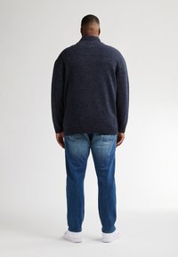 Mörkblå stickad tröja med ribbat krage och detalj på axlarna, parat med ljusblå jeans. Tröjan har en lös passform och strukturerad tyg.