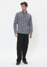 Cămașă cu mâneci lungi de culoare gri, cu un model floral negru, având guler și închidere cu nasturi, asortată cu pantaloni negri și pantofi închisi la culoare.