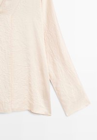 Helles rosa Langarmshirt mit einer zerknitterten Textur, das über einen V-Ausschnitt und subtile Nähte an den Rändern verfügt. Der Saum ist leicht gewellt.