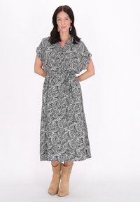 Rochie cu model Paisley alb-negru, cu guler, mâneci scurte, talie strânsă și tiv până la gleznă, asortată cu cizme cowboy bej.