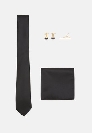 Cravatta nera in seta, fazzoletto da taschino in seta nera e gemelli tono oro con accenti circolari neri, disposti su uno sfondo bianco.