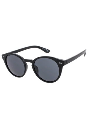 Gafas de sol redondas negras con lentes oscuros, montura de plástico y brazos elegantes. Presenta un branding mínimo en el costado. Diseño de puente plano.
