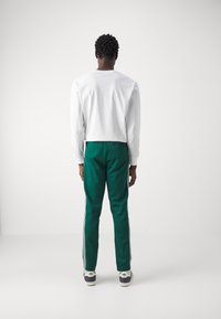 Grønne træningsbukser med hvide sidelister, kombineret med en cropped hvid langærmet trøje. Stoffet ser glat og let ud.