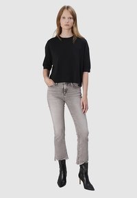 Schwarzes, kurzärmeliges, kurzes Oberteil kombiniert mit hellgrauen, hochtaillierten Jeans mit ausgefransten Säumen und schwarzen knöchelhohen Stiefeln mit Absatz.