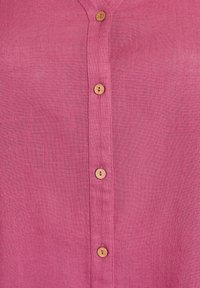 Camicia di lino rosa con una finitura testurizzata e un'apertura corta con quattro bottoni in legno. Il tessuto ha una qualità leggera e traspirante.