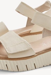 Beige leather platform sandals with wide adjustable straps and a textured sole for added grip and comfort.