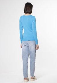 Maglione tricotto azzurro chiaro con maniche lunghe, scollatura rotonda e orlo a costine, abbinato a jeans in denim chiaro a vita alta e sandali beige spessi.