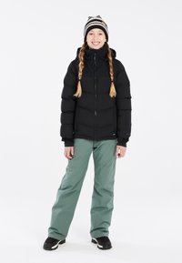 Doudoune noire, avec une fermeture �éclair à l'avant et une capuche ; associée à un pantalon vert ample et des bottes d'hiver noires. Un bonnet tricoté rayé accentue le style.