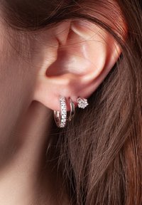 Srebrne kolczyki z trzema nałożonymi obręczami, z których dwie mają przezroczyste kamienie szlachetne oraz mały wkręt w kształcie kwiatu z kamieniem szlachetnym w środku.