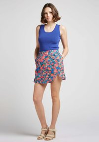 Débardeur bleu à côtes associé à une mini jupe florale présentant des motifs roses, bleus et verts. Le mannequin porte des sandales à talons beiges.