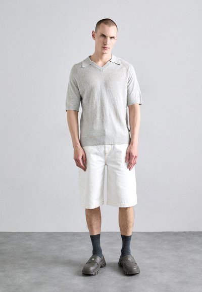 Chemise en tricot gris clair à manches courtes et col en V, associée à un short blanc jusqu'aux genoux et des chaussettes grises, complétée par des chaussures noires à enfiler.