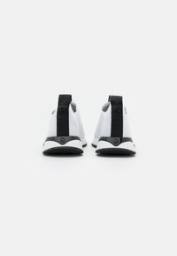 White sneakers with a textured mesh upper, black heel accents, and a flexible sole. Rear view shows logo on heel and sleek design.